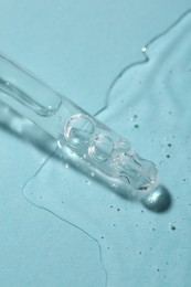 Photo of Dripping cosmetic serum from pipette onto light blue background, macro view