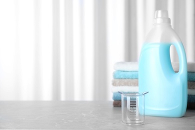 Photo of Measuring cup near bottle of laundry detergent and stacked towels on table. Space for text