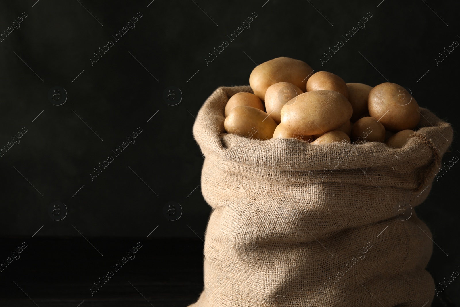 Photo of Raw fresh organic potatoes on black wooden table against dark background. Space for text