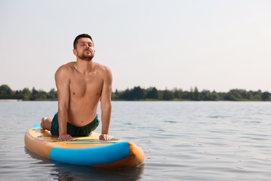 Man practicing yoga on SUP board on river, space for text