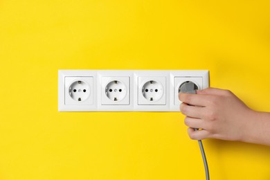 Photo of Woman inserting plug into power socket on yellow wall, closeup. Electrical supply