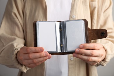 Woman holding leather business card holder with blank cards on grey background, closeup