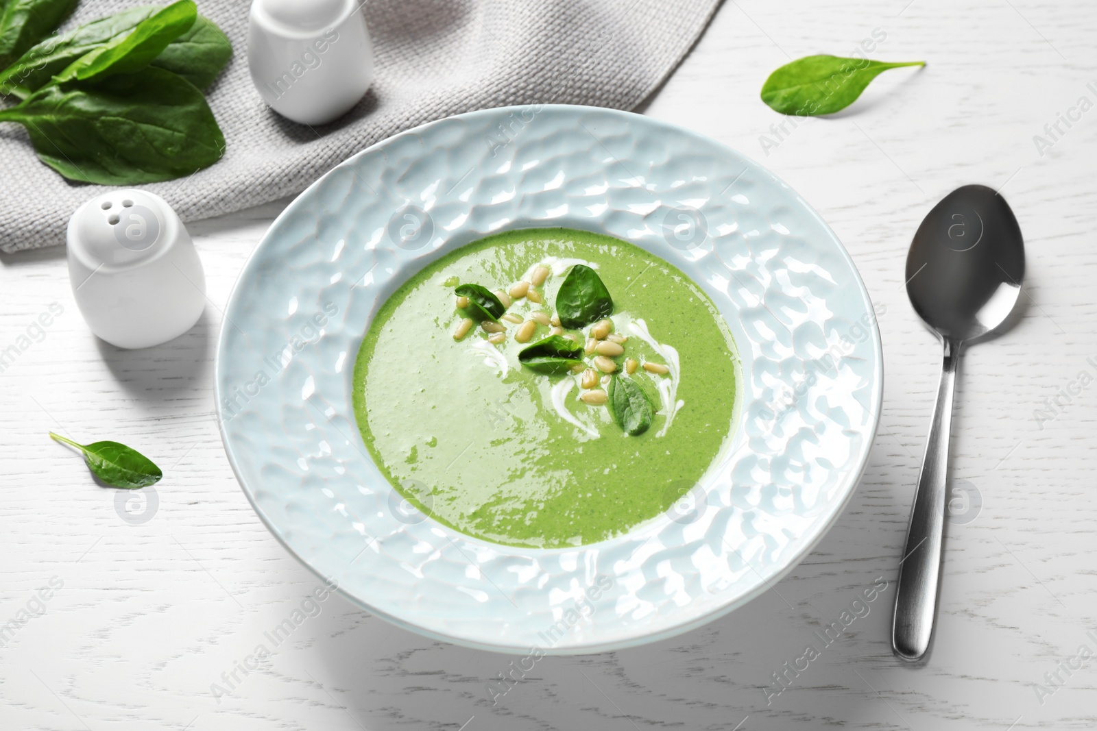 Photo of Plate of healthy green soup with fresh spinach on white wooden table