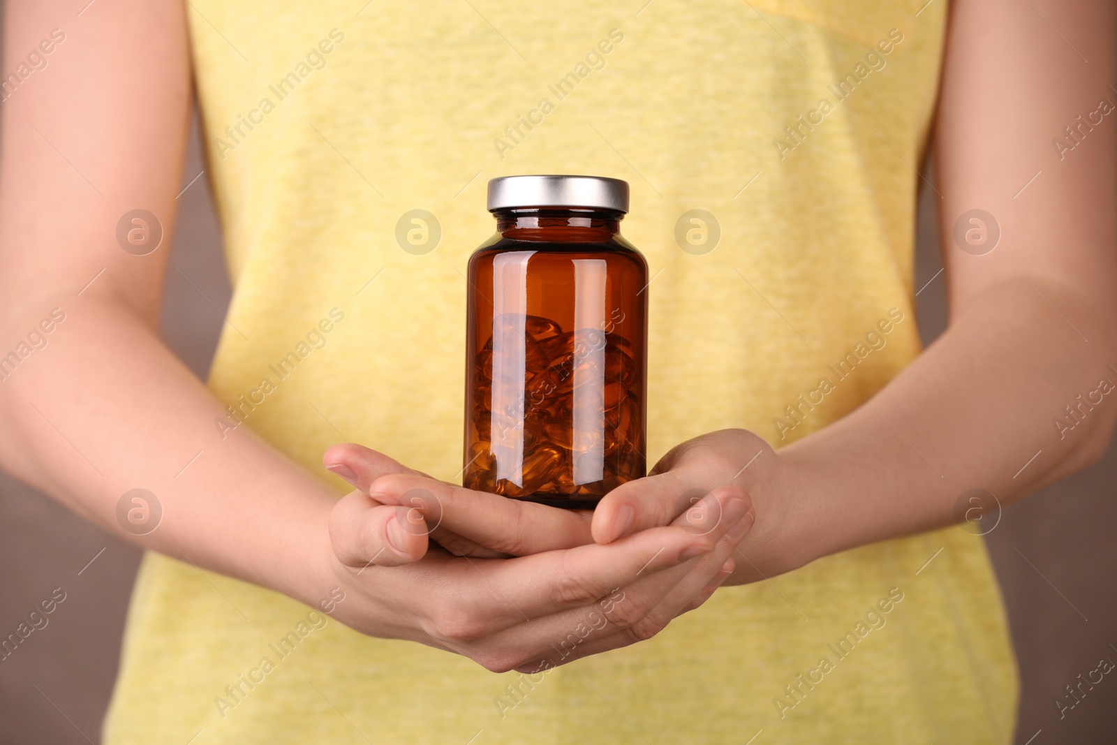 Photo of Woman holding bottle with vitamin capsules against light brown background, closeup