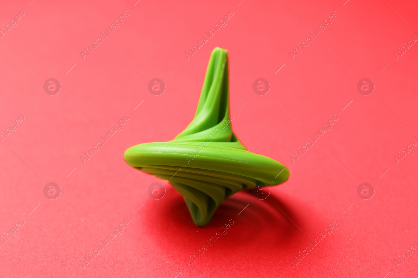 Photo of One green spinning top on red background, closeup