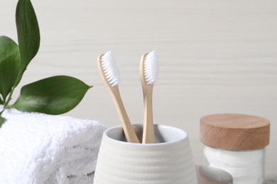 Photo of Bamboo toothbrushes in holder, soft towel and leaves on light background, closeup
