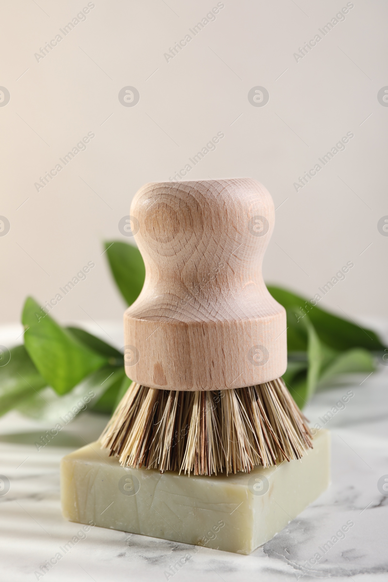 Photo of One cleaning brush and bar of soap on white marble table, closeup