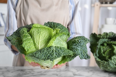 Photo of Woman holding fresh green savoy cabbage over white marble table, closeup