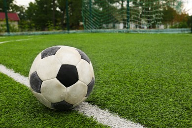 Dirty soccer ball on green football field, space for text