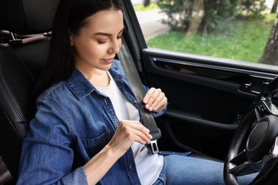 Woman fastening safety seat belt inside modern car