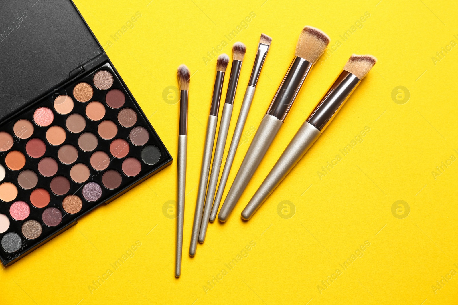 Photo of Flat lay composition with professional makeup brushes and eye shadow palette on yellow background