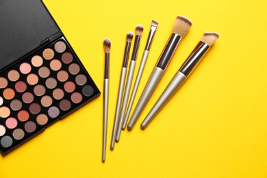 Flat lay composition with professional makeup brushes and eye shadow palette on yellow background