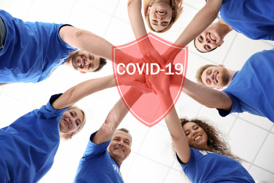 Image of Volunteers uniting to help during COVID-19 outbreak. Group of people holding hands together on light background, shield illustration