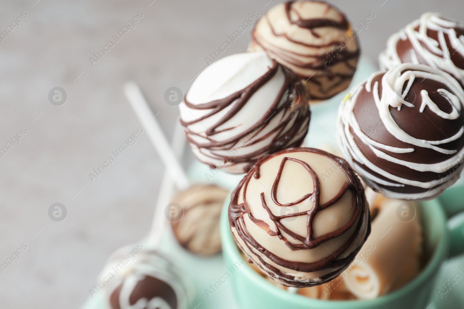 Photo of Yummy cake pops coated with chocolate in cup on table, closeup. Space for text