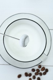 Mini mixer (milk frother), whipped milk and coffee beans on white wooden table, flat lay