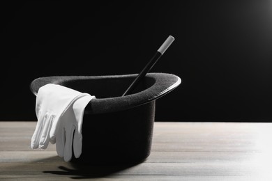 Photo of Magician's hat, gloves and wand on white wooden table against black background, space for text