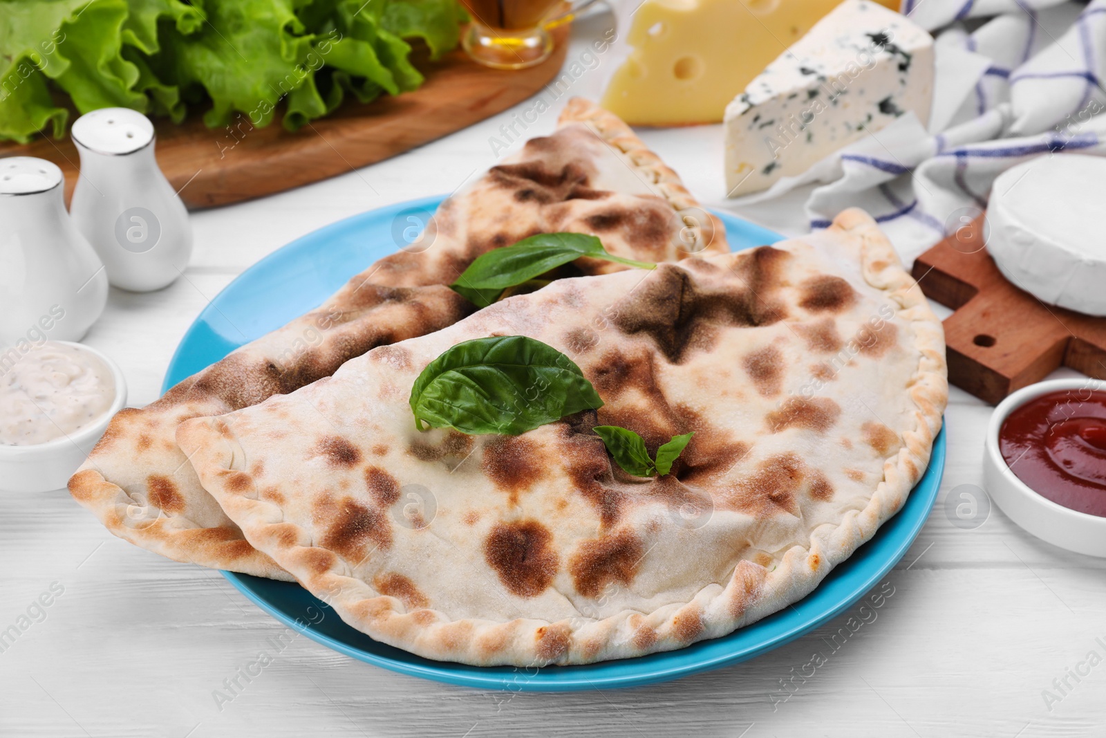 Photo of Delicious cheese calzones and products on white wooden table, closeup