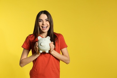 Young woman with piggy bank on color background, space for text. Money saving