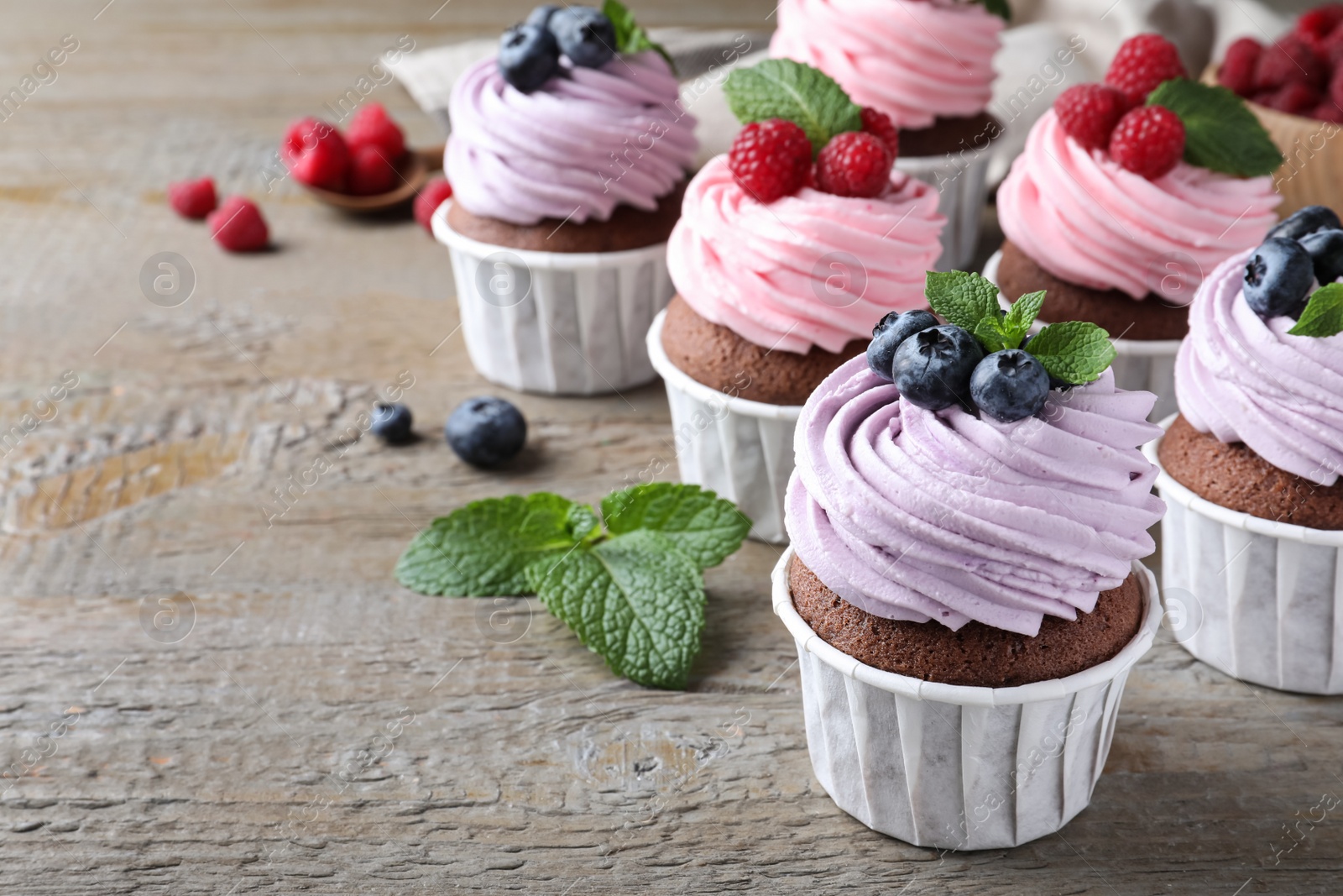 Photo of Sweet cupcakes with fresh berries on wooden table. Space for text