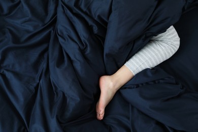 Woman sleeping in comfortable bed with dark blue linens, closeup of leg