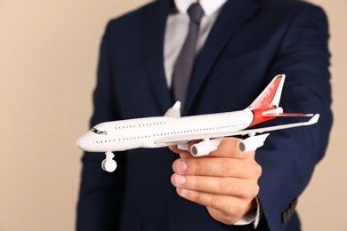 Photo of Insurance agent holding toy plane on color background, closeup. Travel safety concept