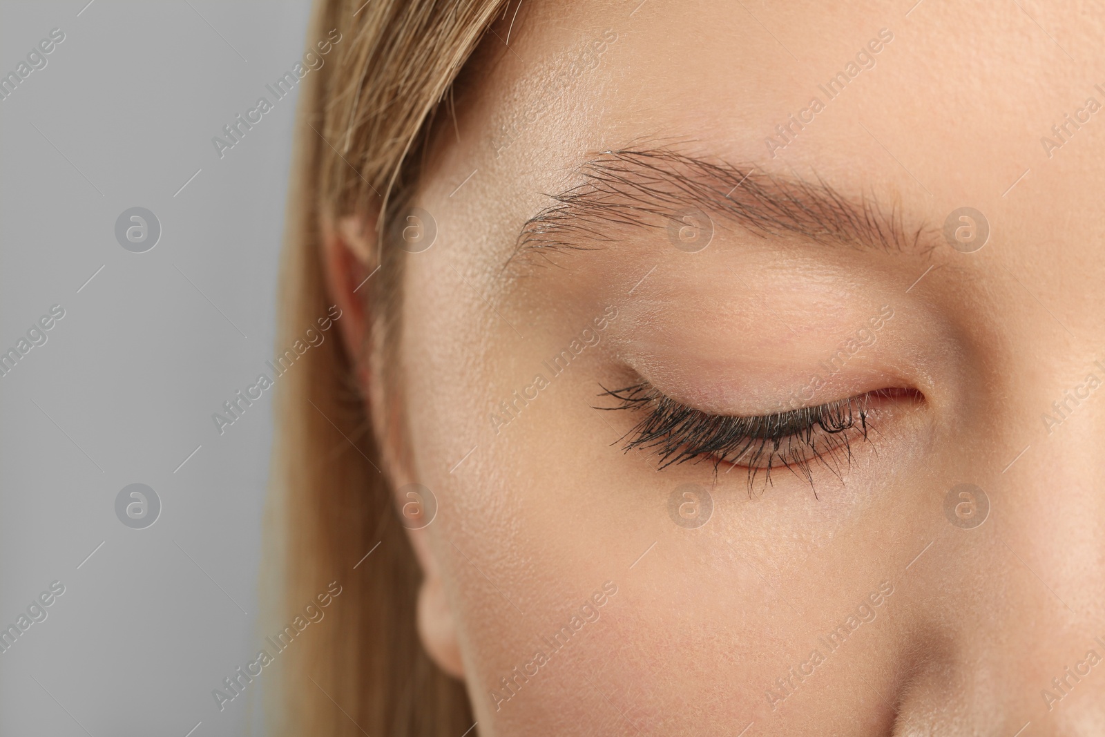 Photo of Woman with long eyelashes after mascara applying against grey background, closeup