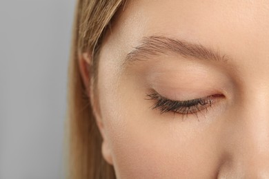 Woman with long eyelashes after mascara applying against grey background, closeup