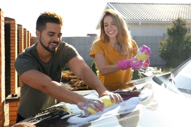 Photo of Happy young couple washing car at backyard on sunny day