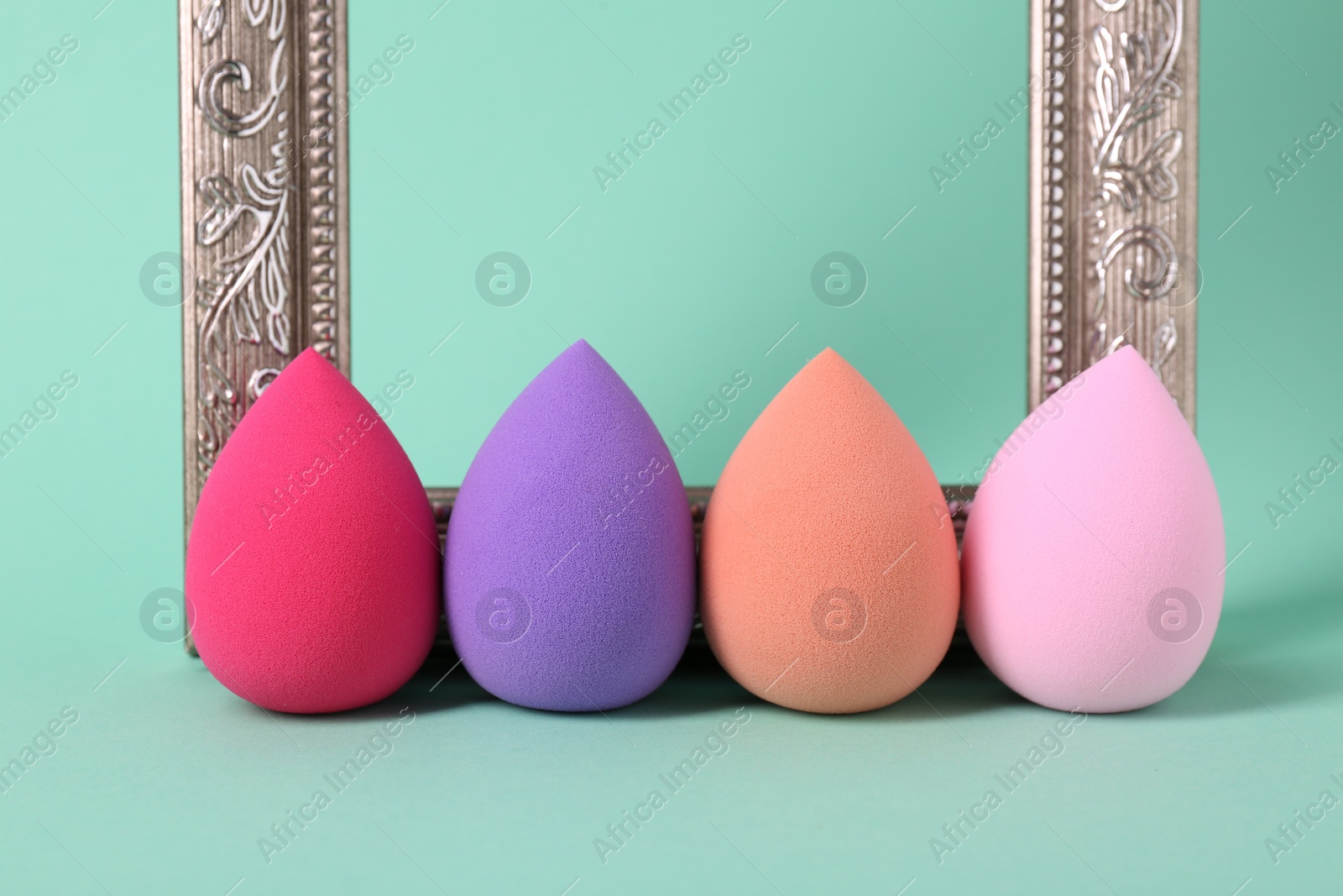 Photo of Colorful makeup sponges and frame on mint color background