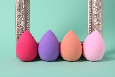 Photo of Colorful makeup sponges and frame on mint color background