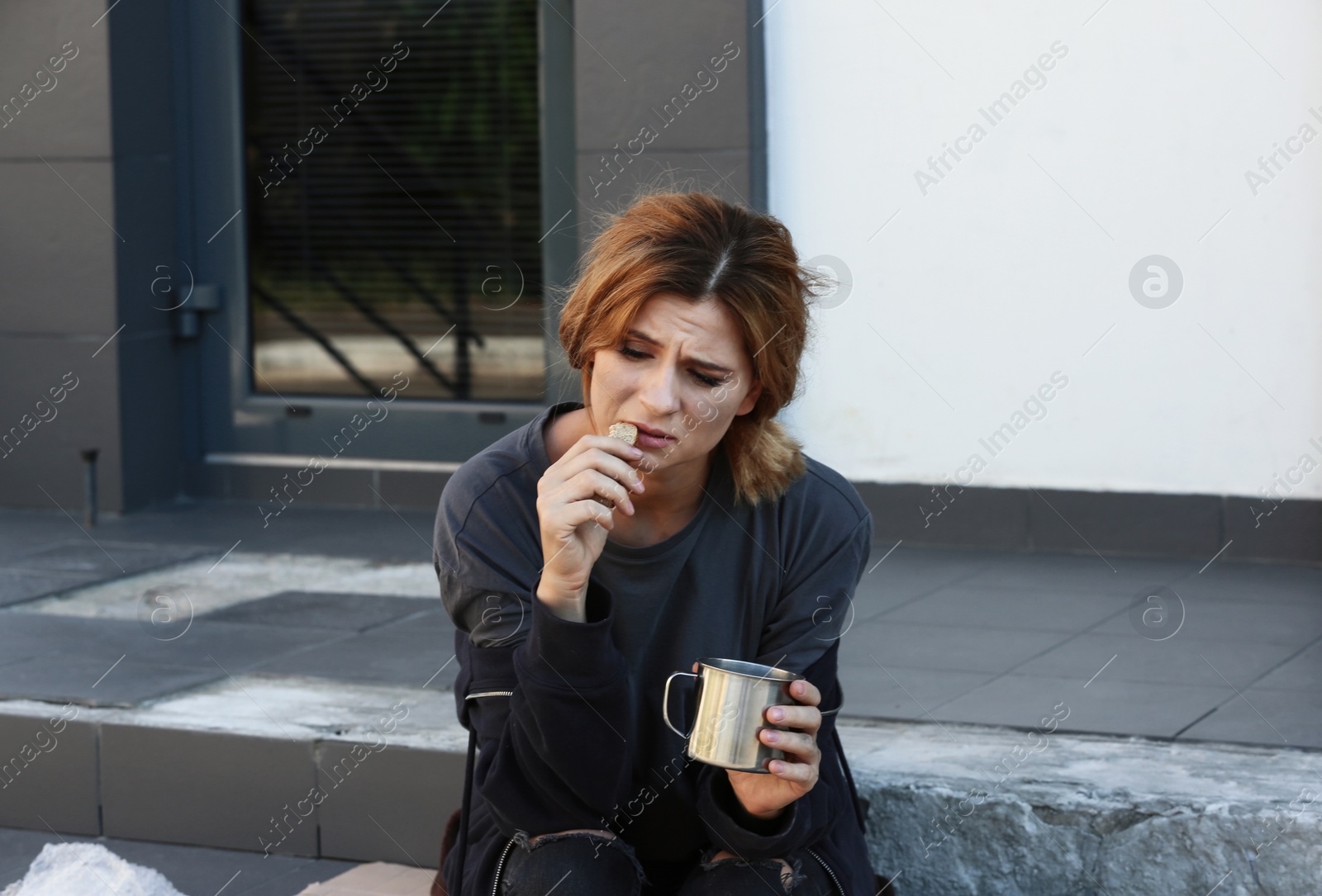 Photo of Poor woman with piece of bread and mug on city street