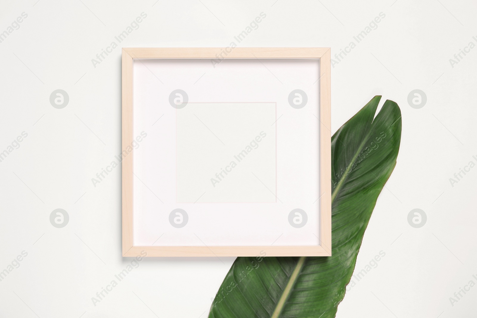 Photo of Empty photo frame and green leaf on white background, top view. Space for design