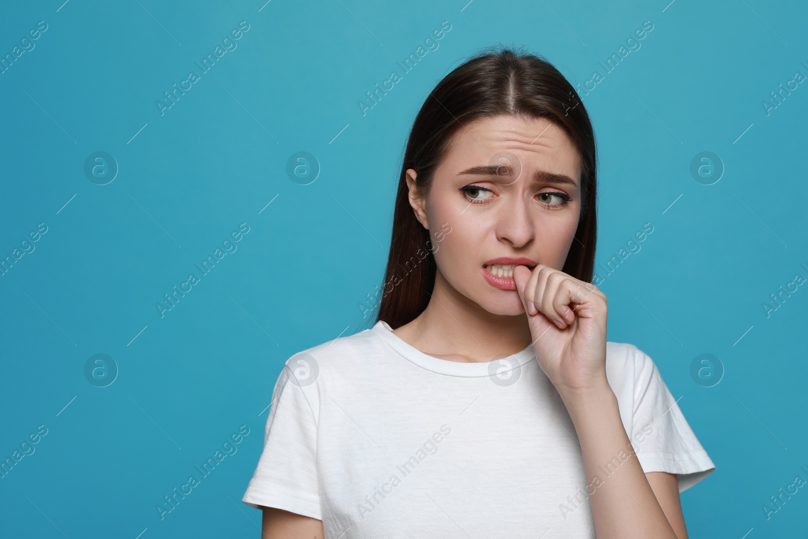 Photo of Young woman biting her nails on light blue background. Space for text