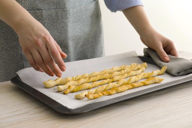 Woman near baking sheet with homemade breadsticks at white wooden table, closeup. Cooking traditional grissini
