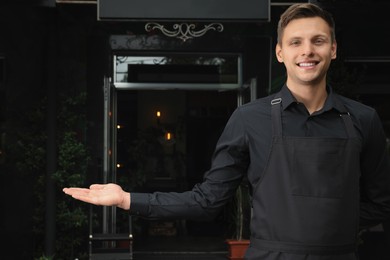 Photo of Happy young waiter in uniform near cafe