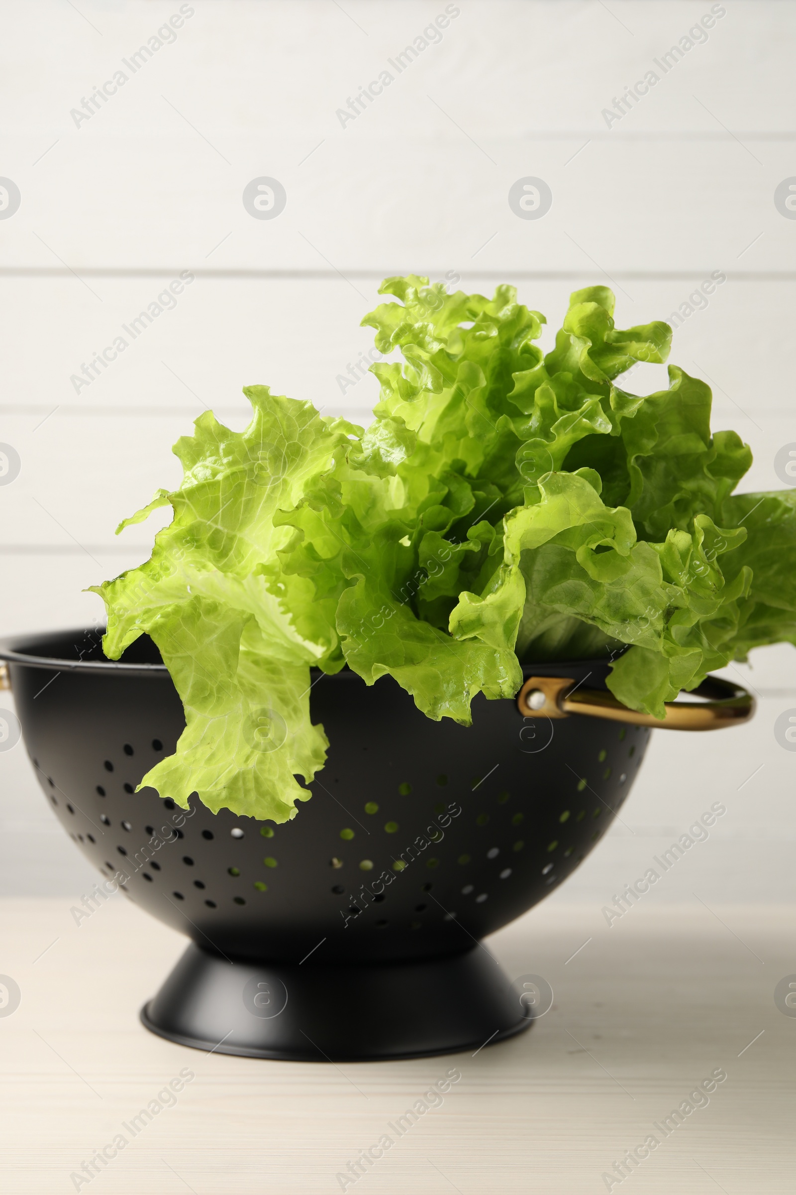 Photo of Fresh lettuce in black colander on white wooden table