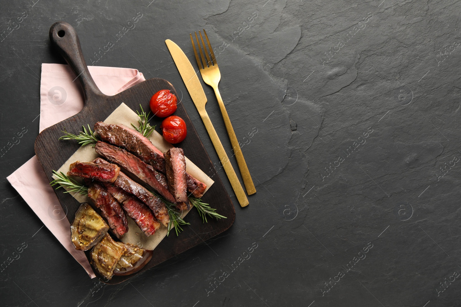 Photo of Delicious grilled beef with vegetables and rosemary served on dark gray table, top view. Space for text