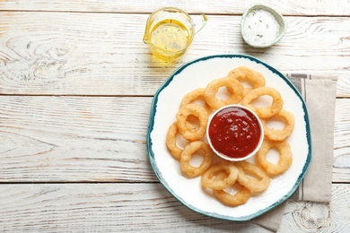 Plate with fried onion rings and sauce served on table, top view