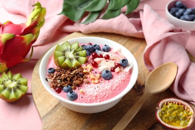 Tasty smoothie bowl with fresh kiwi fruit, berries and granola on pink wooden table