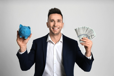 Photo of Happy man with cash money and piggybank on light grey background
