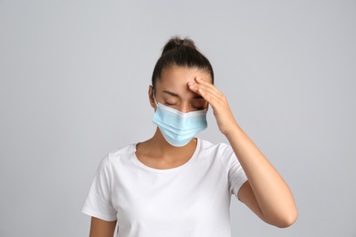 Stressed woman in protective mask on grey background. Mental health problems during COVID-19 pandemic