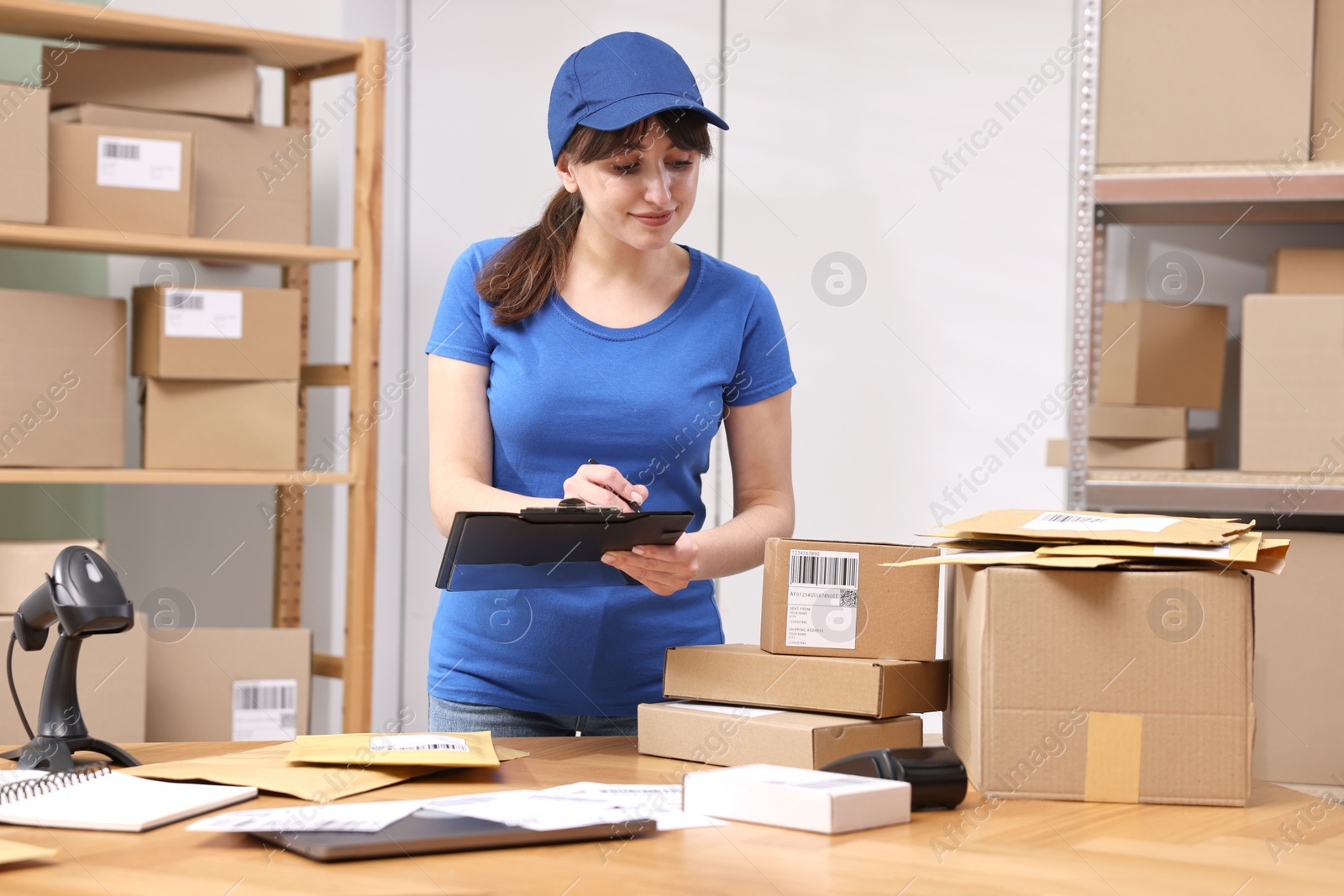 Photo of Parcel packing. Post office worker with clipboard at wooden table indoors