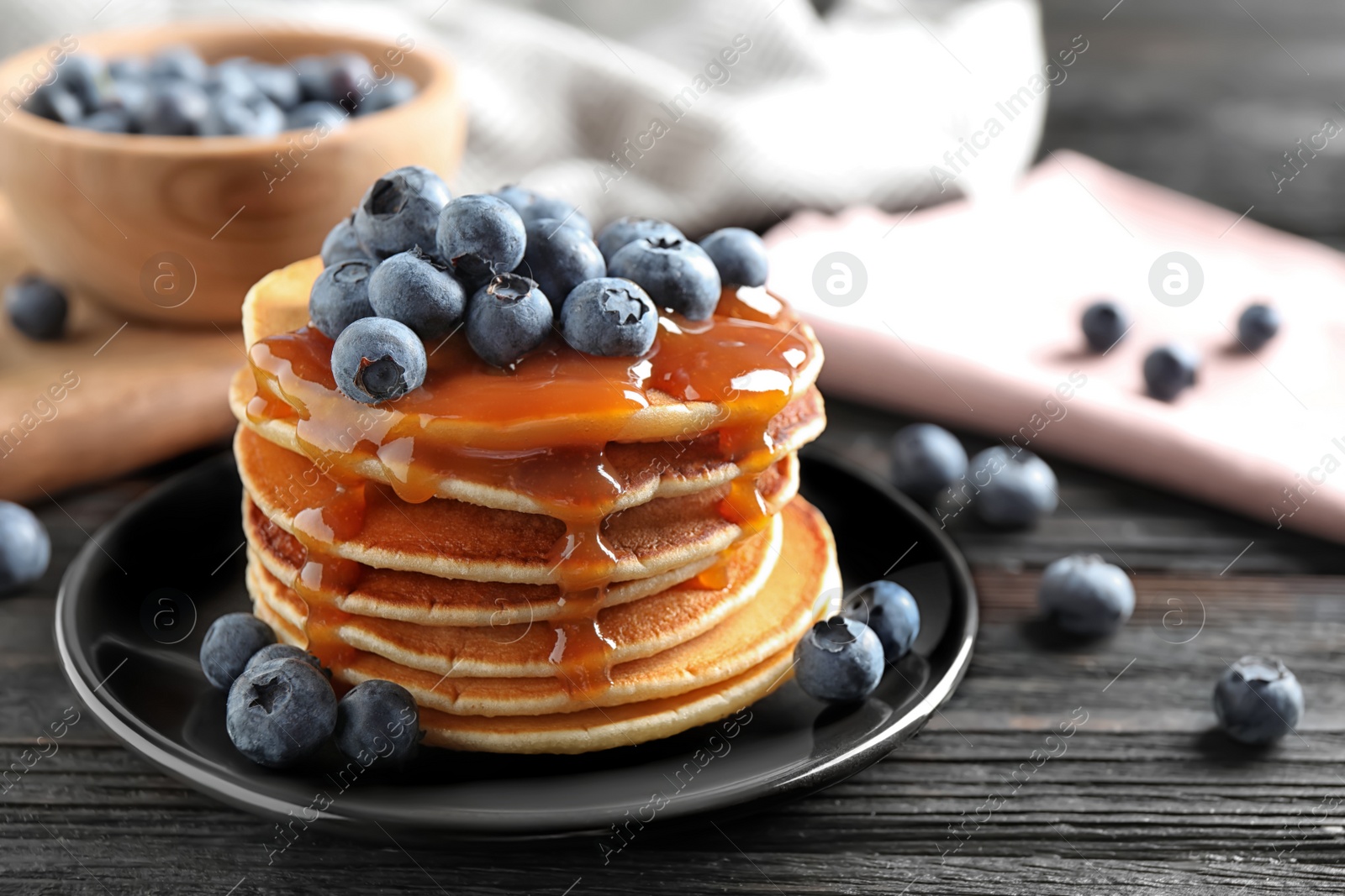 Photo of Delicious pancakes with fresh blueberries and caramel syrup on black wooden table