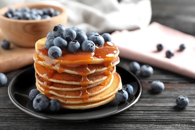 Delicious pancakes with fresh blueberries and caramel syrup on black wooden table