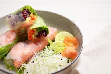 Delicious spring rolls wrapped in rice paper on white wooden table, closeup