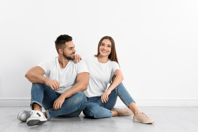 Photo of Young couple in stylish jeans sitting near white wall