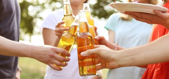 Image of Friends with bottles of beer and food outdoors, closeup. Banner design