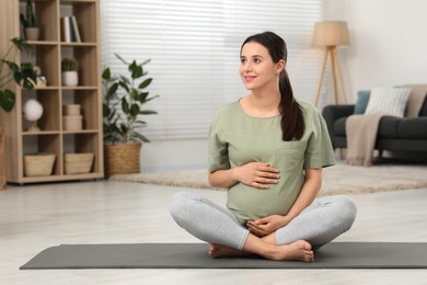 Beautiful pregnant woman sitting on yoga mat at home