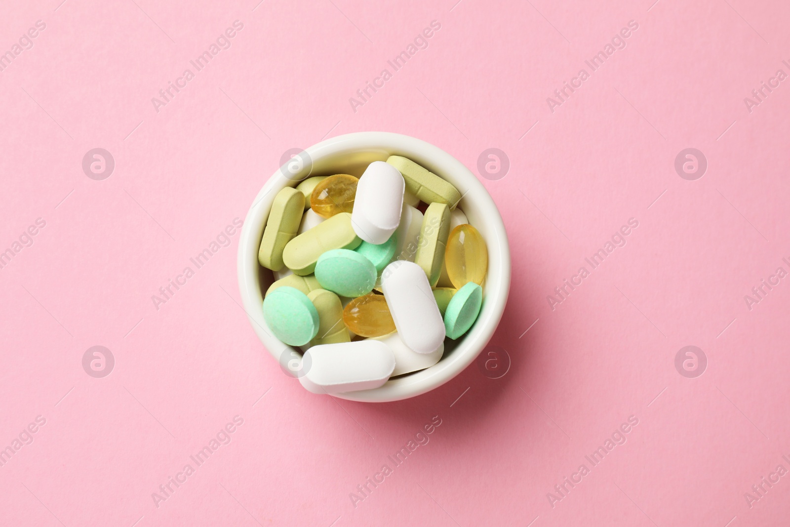 Photo of Different vitamin pills in bowl on pink background, top view