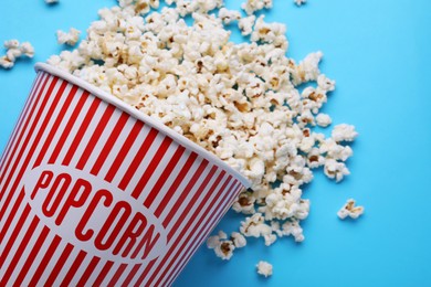 Photo of Overturned paper bucket with delicious popcorn on light blue background, flat lay